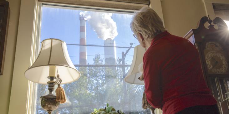 Woman looking out window at smokestacks next to her house