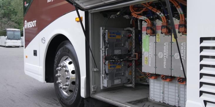 The side compartment of an electric transit bus is open, revealing battery packs, power modules, and orange high‑voltage cables inside.