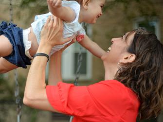 White woman swinging her baby in the air above her head
