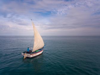 Backed by an empty horizon, a single sailboat takes to the open waters in Cabo Blanco, Peru
