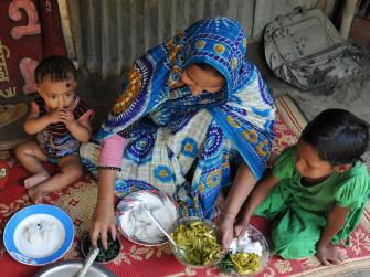 A Bangladeshi woman shares a fish dinner with two young children
