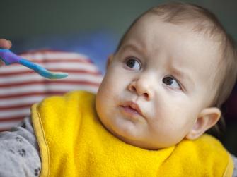 A baby refusing to eat from an offered spoon