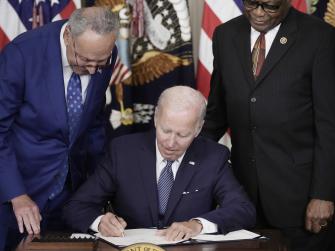 President Joe Biden signs the Inflation Reduction Act while Senator Chuck Schumer and Representative Jim Clyburn look on