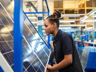 Side view of a female employee inspecting newly manufactured solar panels in company. Woman quality engineer examining solar panels in factory.