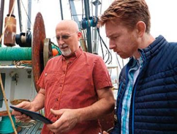 Oregon fisherman Brad Pettinger and EDF's Shems Jud looking at a tablet device on a fishing boat