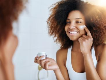 Woman putting on face cream while looking in a mirror