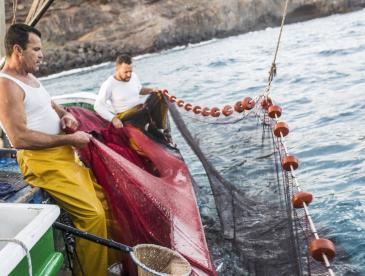 two men work the nets on a fishing boat off the Spain coast