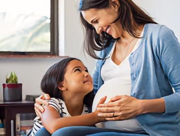 Pregnant mom smiling at a child who is touching her belly