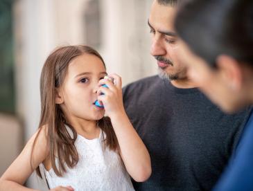 Girl using an asthma inhaler as adults look on
