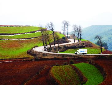 Walmart truck drives up a curved road in a scenic landscape.