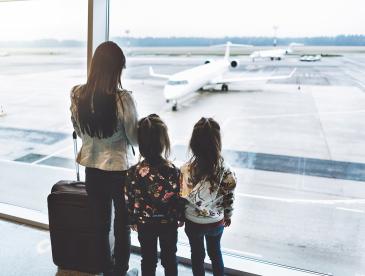 A caregiver with two kids looking out of an airport window at airplanes.