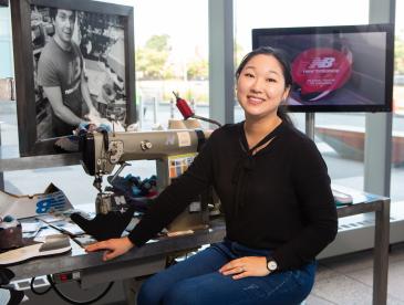 A former Climate Corps fellow inside a brightly lit building, with a screen displaying the New Balance logo. 