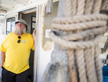 Keith “Buddy” Guindon standing at the door to a fishing boat with a rope tied up in the foreground