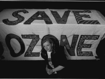 A person sitting in front of a "save ozone" sign.