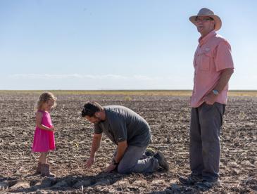 Dwane Roth standing next to his nephew Zion as he digs in the soil. His young daughter stands next to him.