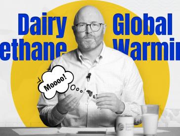 John Tauzel holding a toy cow saying 'moo,' with the words 'dairy methane' and 'global warming' on the screen behind him.