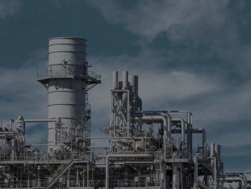 Industrial power generation facility with large metal stacks, pipes, platforms, and cooling structures under a cloudy blue sky.