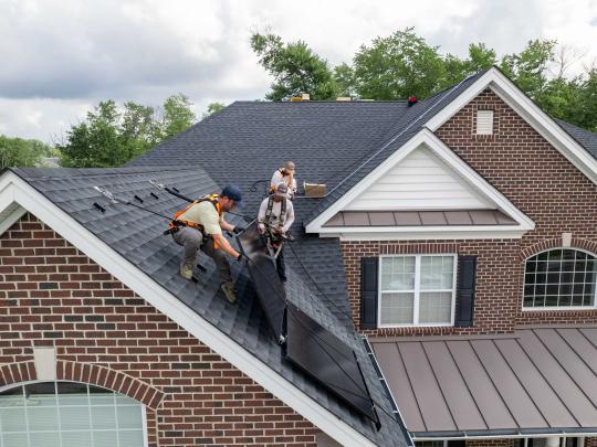 Workers installing solar panels on roof of suburban house