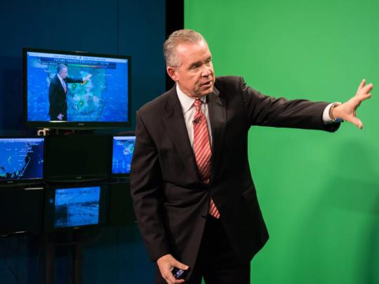 John Morales standing in front of a greenscreen doing the weather.