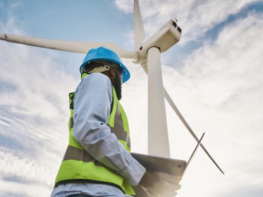 Worker in bright blue hard hat standing beneath a wind turbine.