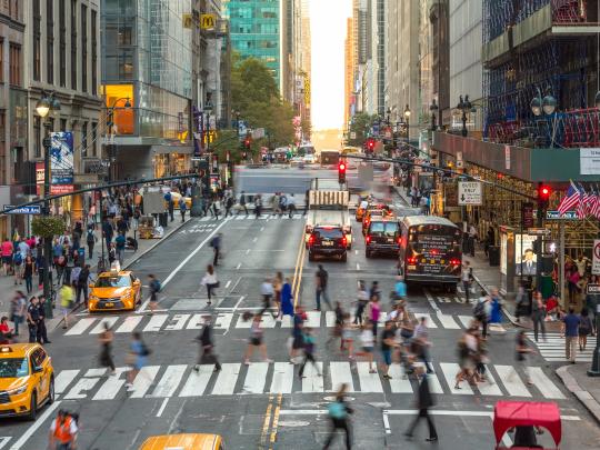 People crossing at a crosswalk in a bit of timelapse blur on a sunny New York City street.