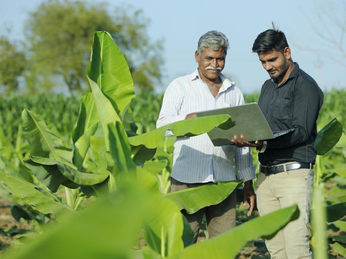 Two men standing in a field examining agricultural data on a computer