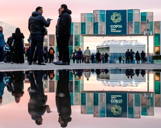 People chat outside a building displaying a teal COP29 banner.