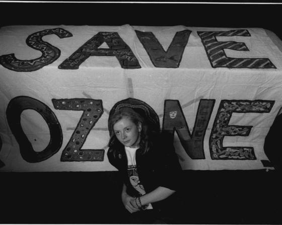 A person sitting in front of a "save ozone" sign.