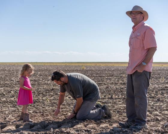 Dwane Roth standing next to his nephew Zion as he digs in the soil. His young daughter stands next to him.