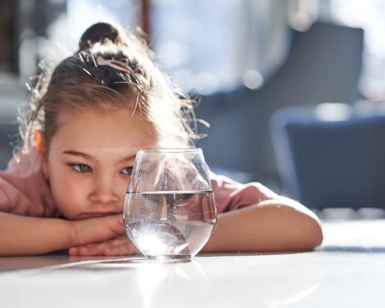 A small child looking at a glass of water.