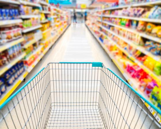 A shopping cart going down a colorful aisle at the grocery store.
