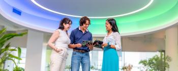 3 young people standing in a lobby looking excitedly at a magazine