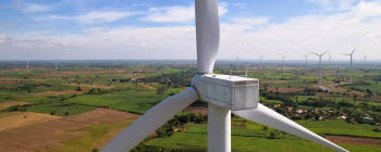 A giant wind turbine with many smaller ones in the distance across farming fields