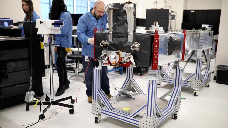 A person wearing gloves adjusts a large piece of equipment in a lab setting.