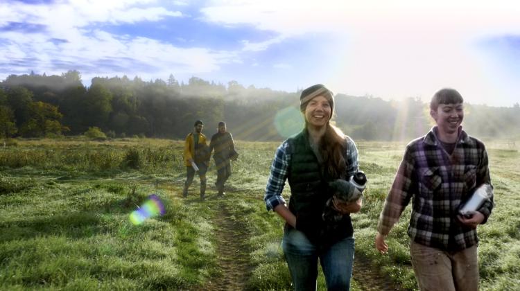Two pairs of people walking across a sunlit field. The people in the  foreground are smiling.